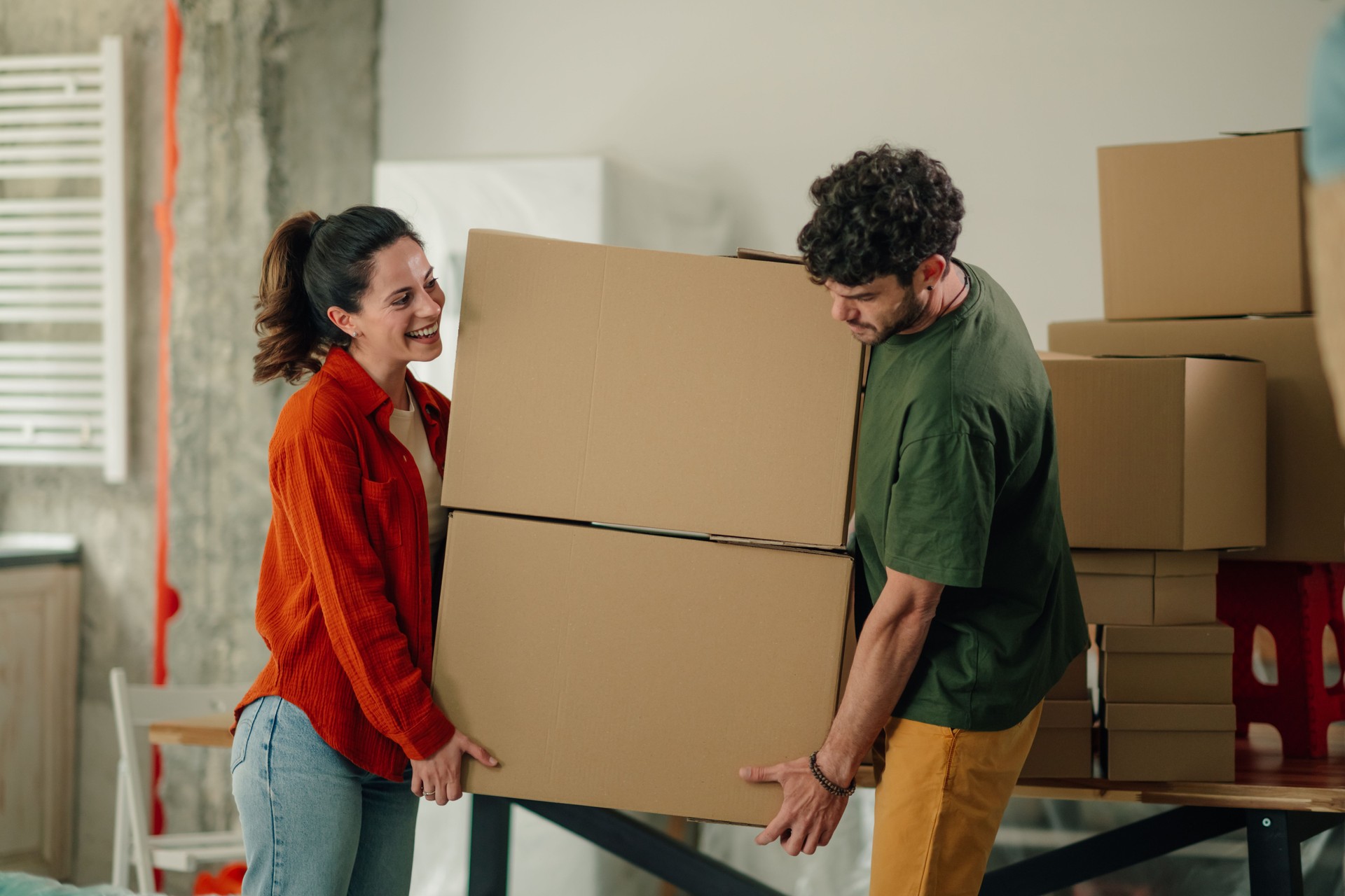 Young couple carrying heavy cardboard boxes into new apartment