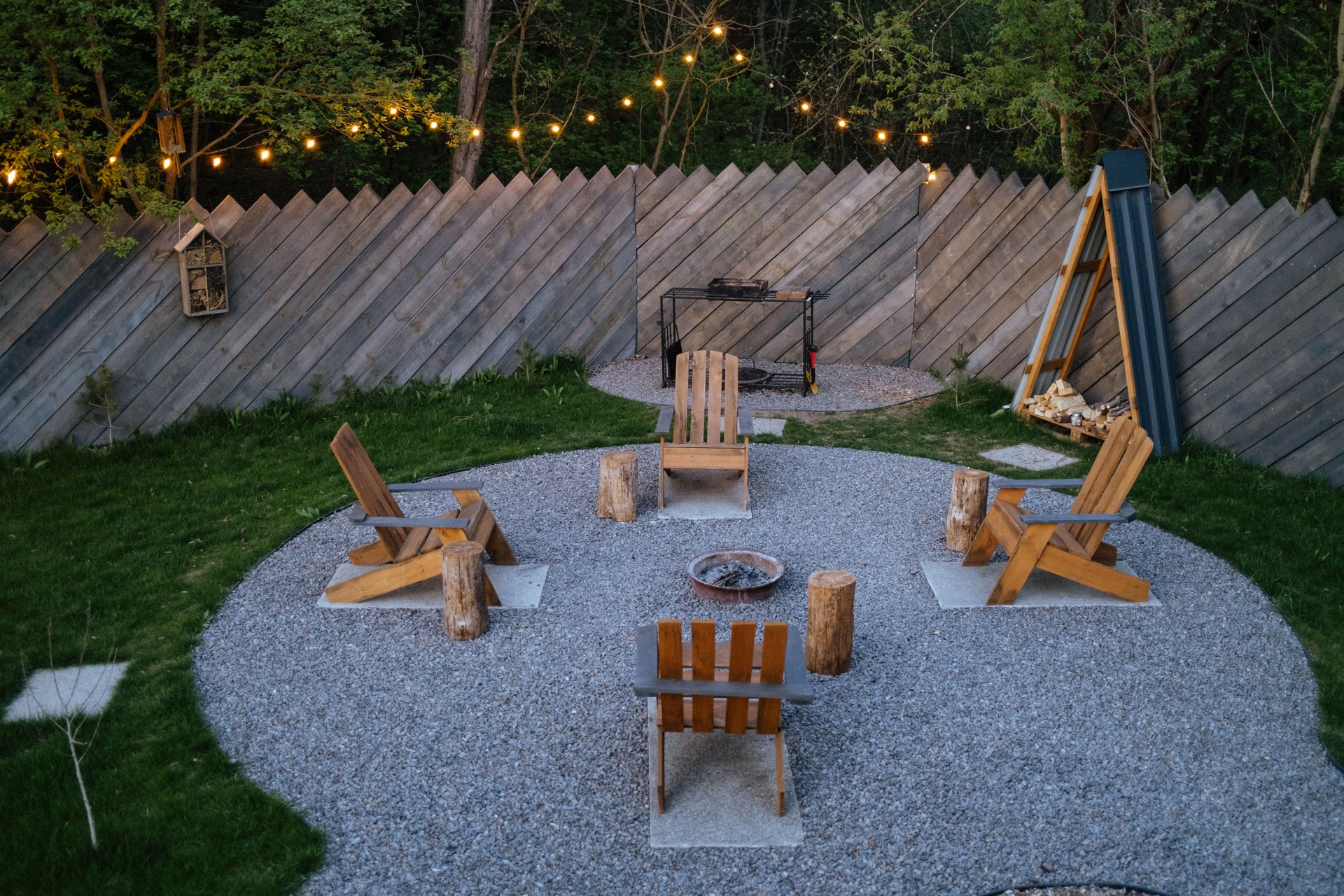 Cozy backyard fire pit area with wooden chairs, string lights, evening gathering